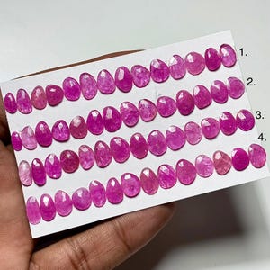 May include: Rows of oval-shaped, faceted pink gemstones are arranged on a white card. The gemstones vary in size and shade, ranging from light pink to deep magenta. The card is labeled with numbers 1 through 4.