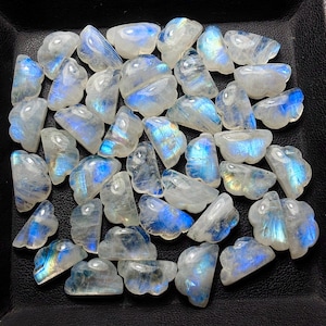 Pode incluir: Uma coleção de pedras preciosas de pedra da lua polidas. As pedras são em sua maioria translúcidas com uma base branca leitosa e flashes iridescentes azuis e amarelos. As formas variam, algumas parecem pequenas nuvens irregulares.