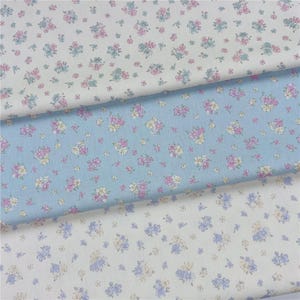 Könnte beinhalten: Drei Stoffmuster mit floralen Mustern. Eines ist hellblau, eines ist weiß und eines ist cremefarben. Die floralen Muster umfassen rosa, lila und gelbe Blumen mit grünen Blättern. Der Stoff ist wahrscheinlich Baumwolle oder ein ähnliches Material.