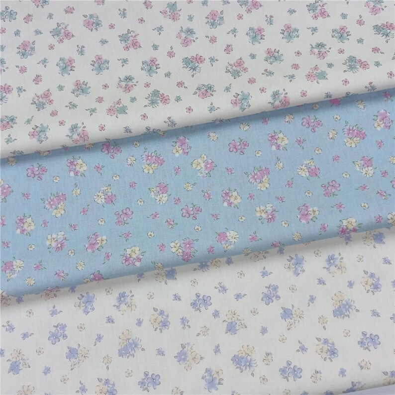 May include: Three fabric swatches with floral patterns. One is light blue, one is white, and one is off-white. The floral patterns include pink, purple, and yellow flowers with green leaves. The fabric is likely cotton or a similar material.