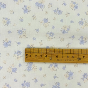 May include: White fabric featuring a floral design in pale blue and cream hues. A wooden ruler with centimetre markings is placed on the fabric, showing measurements up to 11 cm.