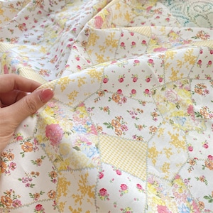 Könnte beinhalten: Weißer Stoff mit Patchwork-Muster mit gelben und rosa Blumenmustern. Der Stoff hat eine gesteppte Optik und ist perfekt für Bastelarbeiten.