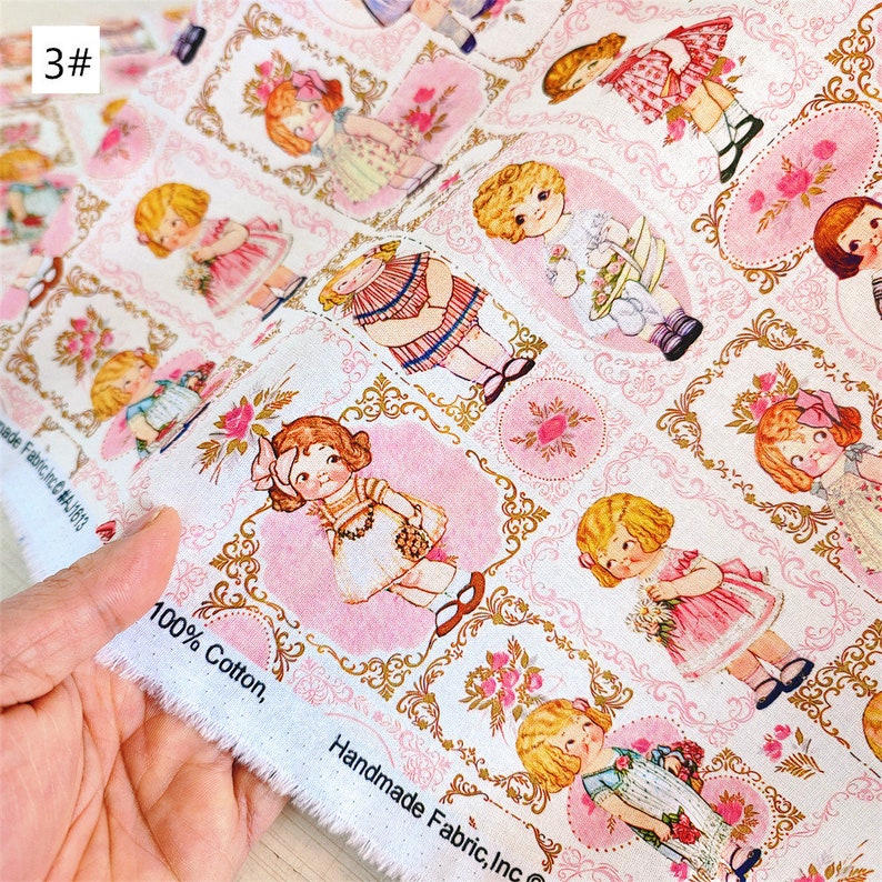 May include: White cotton fabric with a repeating pattern of girls in pink dresses and gold frames. The fabric has the text "100% Cotton, Handmade Fabric, Inc." printed on the edge.