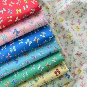 May include: A collection of colorful fabric swatches featuring a repeating pattern of small bows. The fabrics are in shades of red, pink, blue, green, and yellow, with the bows in various colors. The fabric on the right is a cream color with a similar bow pattern.
