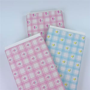 May include: Three folded sheets of patterned paper. One is pink with strawberries, another is pink with cherries, and the third is light blue with lemons. Each sheet has a white border and a plaid design.