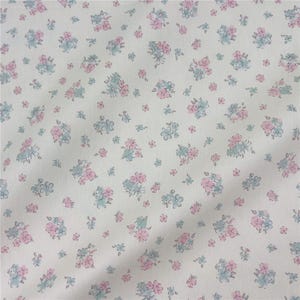 May include: White fabric featuring a repeating pattern of small pink and blue floral bouquets. The flowers are scattered across the surface, creating a delicate design. The fabric has a soft, slightly textured appearance.