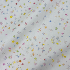 May include: White fabric featuring a pattern of watercolour stars in multiple colours, such as yellow, blue, pink, and orange. The stars vary in size and are spread across the fabric. The fabric has a soft, slightly textured appearance.