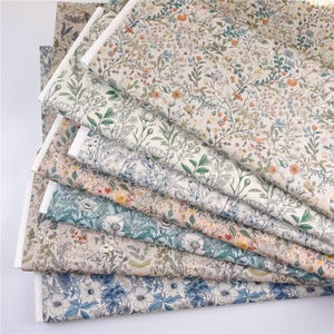 May include: A selection of floral fabric samples in various colours. The fabrics feature detailed botanical patterns with flowers, leaves, and vines in shades of blue, green, pink, and beige. The edges of the fabric are white.