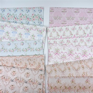 May include: A collection of rectangular fabric sheets featuring various floral patterns in shades of pink, blue, and cream. The designs include repeating motifs of roses, ribbons, and ornate trellis patterns arranged in horizontal rows across the fabric.