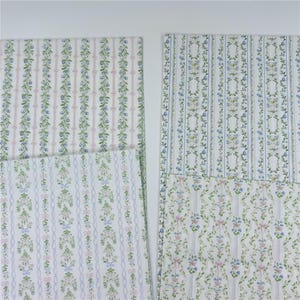 May include: Four rectangular sheets of paper featuring vertical patterns of green vines, small blue flowers, and pink or light blue ribbons on a white background. The designs include repeating floral garlands and delicate striped motifs.