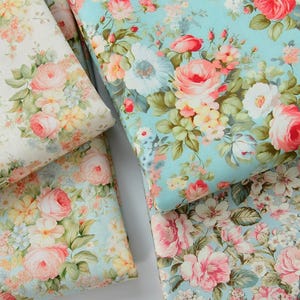 May include: Close-up of several fabric samples featuring floral patterns. The fabrics display a variety of flowers in shades of pink, red, yellow, and white, set against light blue and cream backgrounds. The floral designs are detailed and create a vintage aesthetic.