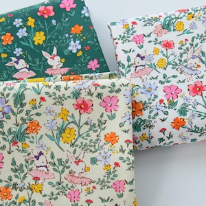 May include: Close-up of three fabric swatches with floral and bunny ballerina patterns. The fabrics feature a variety of colorful flowers in pink, orange, yellow, and blue, with green foliage. The bunnies are wearing tutus. The background is white, green, and cream.