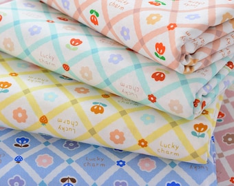 May include: Stack of four fabric squares with a checkered pattern and a repeating design of flowers, strawberries, and the text "Lucky charm".