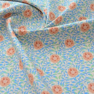 Op de afbeelding: Een close-up van een stof met een herhalend patroon van oranje bloemen en blauwe bladeren op een cr&egrave;me achtergrond.