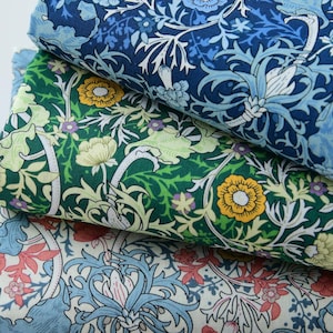 May include: Three stacks of patterned fabric in shades of blue, green, and cream. The fabric features floral designs with intricate details in white, yellow, and red. The patterns include flowers, leaves, and swirling vines, creating a vintage aesthetic.