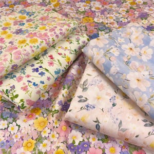 May include: An assortment of floral fabric swatches in various colors. The fabrics feature patterns of pink, yellow, purple, and blue flowers. The swatches are folded and layered, showcasing the different designs and textures of the fabric.