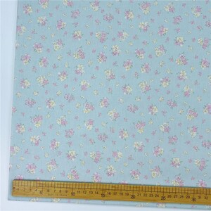 May include: A light blue fabric with a repeating floral pattern. The flowers are pink and yellow. A ruler is along the bottom edge, marked in centimetres.