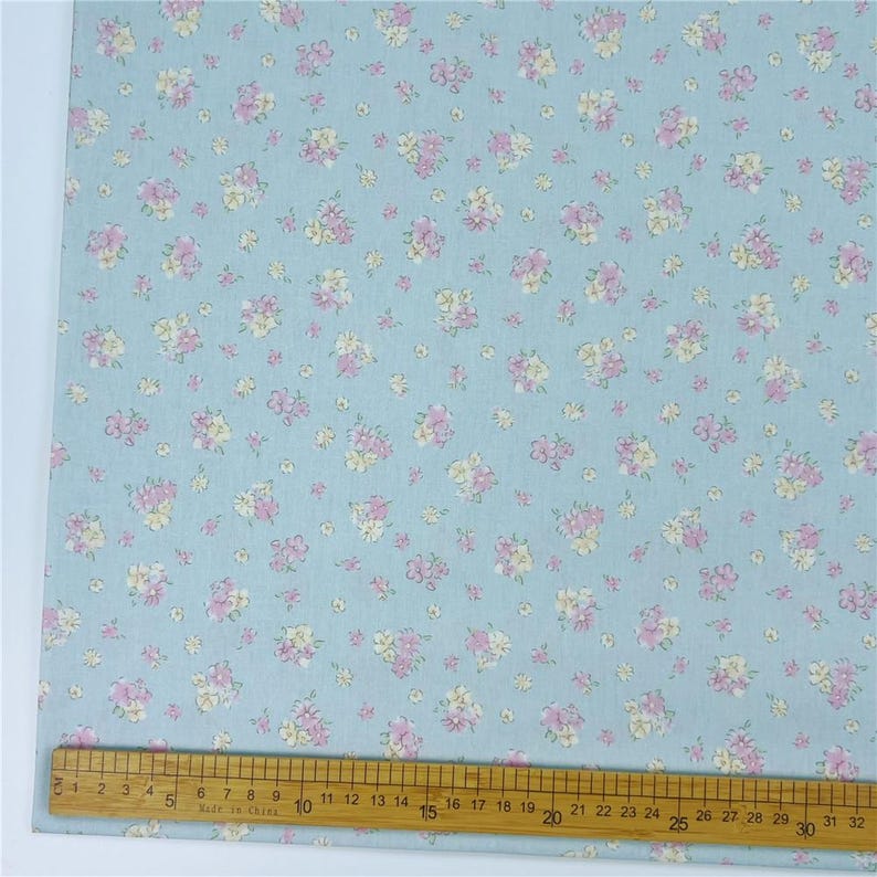 May include: A light blue fabric with a repeating floral pattern. The flowers are pink and yellow. A ruler is along the bottom edge, marked in centimetres.