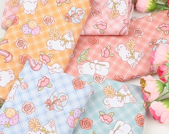 May include: Assortment of fabric featuring a repeating pattern of bears holding flowers and a plaid background. The fabrics are in shades of orange, pink, blue, and green.