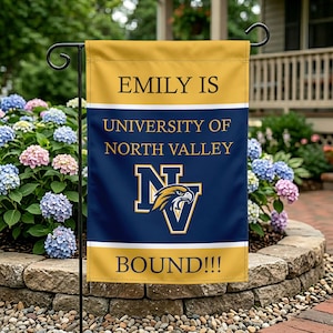 Könnte beinhalten: Eine rechteckige Gartenflagge mit goldenem Ober- und Unterteil und einer marineblauen Mitte. Auf der Flagge steht in goldener Schrift "EMILY IS UNIVERSITY OF NORTH VALLEY BOUND!!!". In der Mitte befindet sich das Logo der Universität.