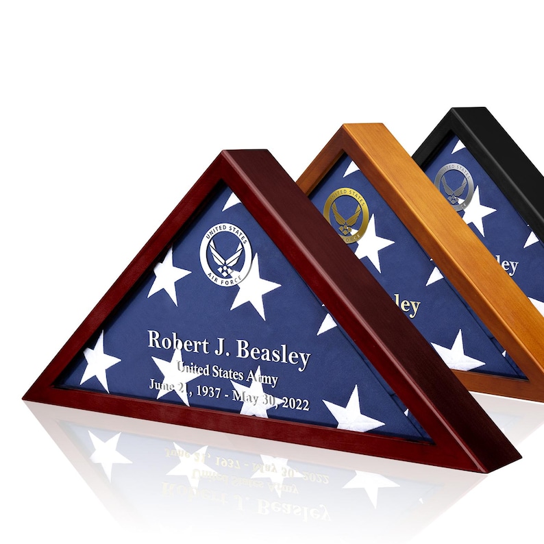 May include: A wooden triangular shadow box with a folded American flag inside. The flag is blue with white stars and has the United States Air Force emblem in the center. The box has a personalized inscription that reads "Robert J. Beasley, United States Army, June 21, 1937 - May 30, 2022".
