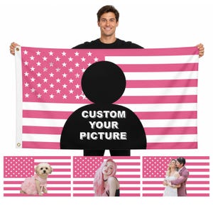 Puede incluir: Una bandera estadounidense rosa y blanca con una silueta negra y el texto "CUSTOM YOUR PICTURE". La bandera está sostenida por una persona. Debajo hay tres banderas más pequeñas con imágenes de un perro, una mujer y una pareja.