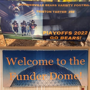 May include: Two banners, one black with orange text and the other blue with orange text. The black banner reads "Summerville Bears Varsity Football,  Triston Tarter #58, Playoffs 2022, Go Bears!" The blue banner reads "Welcome to the Funder Dome!"