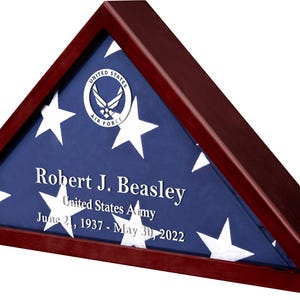 May include: A mahogany wood triangular shadow box with a folded American flag inside. The flag is blue with white stars and has the United States Air Force emblem in the upper left corner. The name "Robert J. Beasley", "United States Army", and the dates "June 21, 1937 - May 30, 2022" are engraved on the flag.