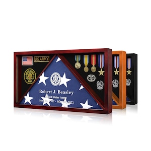 May include: A wooden display case with a folded American flag, medals, and military insignia. The case has a dark wood finish and includes the text "U.S. ARMY" and the name "Robert J. Beasley". Additional cases in orange and black are visible.