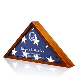 May include: A wooden triangular flag display case with a folded American flag inside. The flag is blue with white stars and has the United States Air Force emblem in the center. The case has a personalized inscription that reads "Robert J. Beasley, United States Army, June 21, 1937 - May 30, 2022".