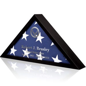 May include: A black triangular shadow box with a folded American flag inside. The flag is blue with white stars and a silver seal. The text "Robert J. Beasley, United States Army, June 21, 1937 - May 30, 2022" is printed on the flag.