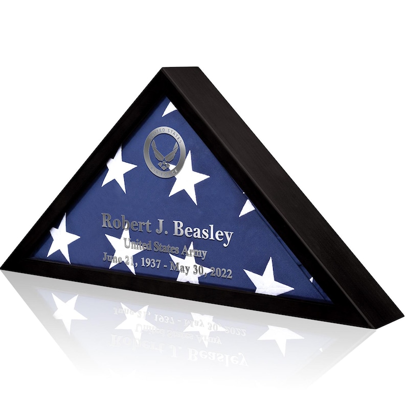 May include: A black triangular shadow box with a folded American flag inside. The flag is blue with white stars and a silver seal. The text "Robert J. Beasley, United States Army, June 21, 1937 - May 30, 2022" is printed on the flag.