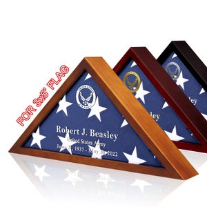 May include: A wooden flag display case with a folded American flag inside. The case is stained a dark wood color and has a gold United States Air Force emblem on the flag. The flag is blue with white stars and has the text "Robert J. Beasley, United States Army, June 21, 1937 - May 30, 2022" printed on it.