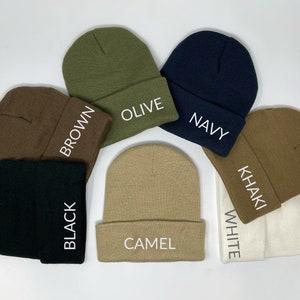 May include: Seven different colored knit beanies with white embroidered text. The colors are olive, navy, brown, black, camel, khaki, and white.