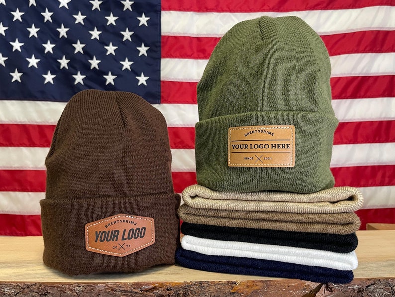 May include: Two brown and green knit beanies with leather patches that say "Brentsbrim's" and "Your Logo Here". The beanies are in front of an American flag.