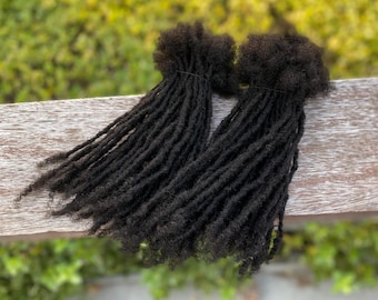 May include: Two bundles of black dreadlocks hair extensions. The dreadlocks are long and thick, and they are arranged in a loose, flowing style.