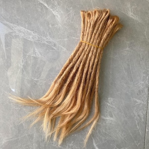 May include: A bundle of light brown synthetic dreadlocks, tied together with a rubber band.