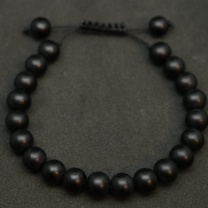 May include: A black beaded bracelet with a black cord closure. The beads are round and matte.