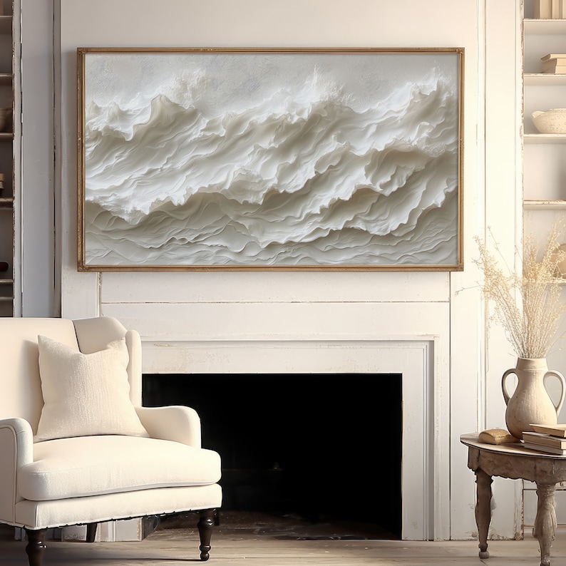 May include: A white and gold framed canvas print of a textured abstract wave design. The print is hanging above a fireplace in a white room.