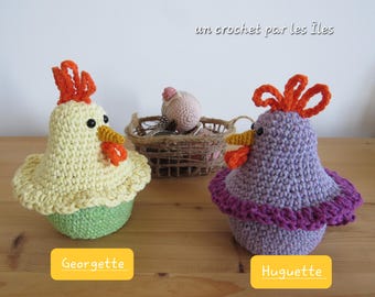 May include: Two crocheted Easter chicks, one yellow with an orange comb and the other purple with an orange comb, are sitting on a wooden surface. The text "un crochet par les îles" is visible in the background.