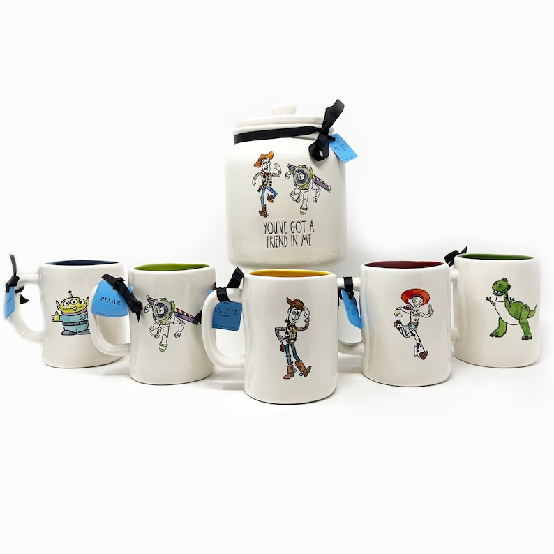 Puede incluir: Conjunto de seis tazas de cer&aacute;mica blanca con personajes de la franquicia de pel&iacute;culas Toy Story. Las tazas tienen bordes y asas de diferentes colores. Las tazas representan a Woody, Buzz Lightyear, Rex, Jessie y un extraterrestre verde. Las tazas est&aacute;n dispuestas en fila sobre una superficie blanca. El texto "You've got a friend in me" est&aacute; impreso en la parte delantera de la taza en el centro de la fila.