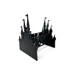 May include: Black decorative castle-shaped shelf. The shelf features a silhouette design of a castle with multiple turrets, flags, and a Mickey Mouse head. The shelf is made of a solid material and has a rectangular base.