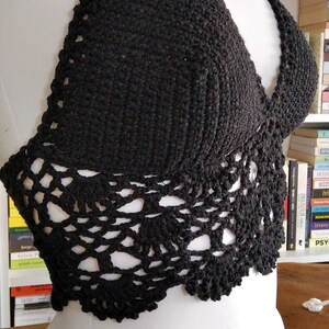 Pode incluir: Um top halter preto de croch&ecirc; com uma delicada borda de renda. O top &eacute; mostrado em um manequim branco.