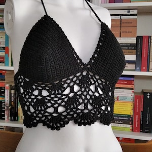 Pode incluir: Um top halter preto de croch&ecirc; com um delicado padr&atilde;o de renda. O top &eacute; exibido em um manequim branco contra um fundo de estante.