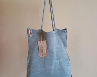 Puede incluir: Una bolsa de mano de punto azul claro con una etiqueta de cuero marrón que dice "Wild Silk Knitting". La bolsa está colgada de un gancho.
