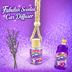 May include: A Fabulux scented car diffuser with a clear glass bottle, a wooden cap, and a hanging rope. The label features a rainbow, flowers, and the text Fabulux. Next to it is a sprig of lavender and a purple bottle with a matching label.