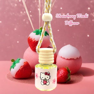 May include: A strawberry mochi diffuser with a Hello Kitty design. The clear glass bottle has a wooden cap and is suspended by a rope. The label features Hello Kitty holding a strawberry. Decorative strawberries and pink spheres surround the diffuser.