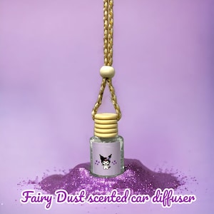May include: A small glass bottle with a purple glitter design and a cartoon character on the label. The bottle is hanging from a string with a wooden bead. The bottle is surrounded by purple glitter. The text "Fairy Dust scented car diffuser" is written below the bottle.