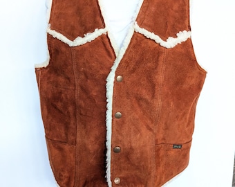 May include: A brown suede vest with a white faux fur lining. The vest has a snap closure and two pockets.