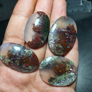Puede incluir: Cuatro cabujones de ágata de forma ovalada con un patrón verde musgo, marrón y blanco. Los cabujones son translúcidos y tienen un acabado pulido.